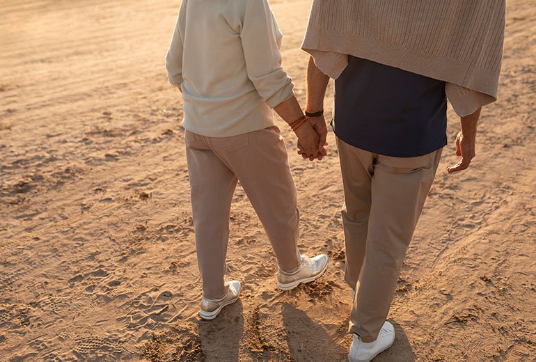 Image d'un couple de retraités marchant main dans la main sur une plage, symbole de la retraite heureuse.