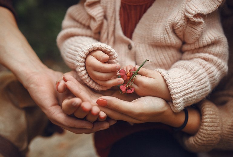 Vue rapprochée de la main d'un bébé tenant une fleur, symbolisant la planification successorale familiale avec ses parents.